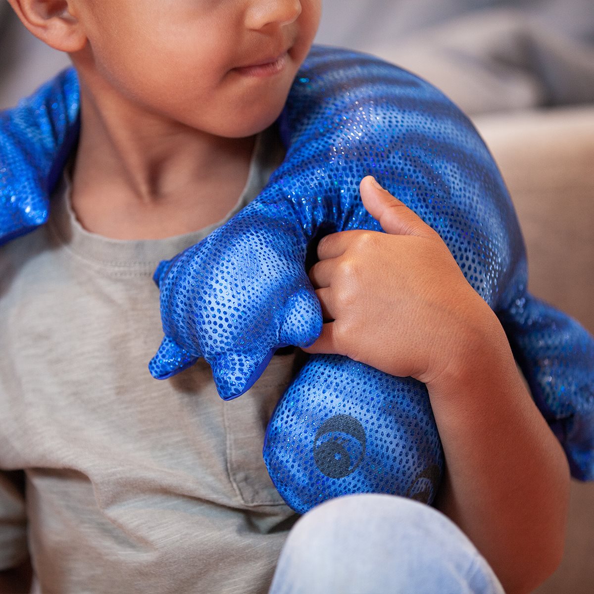 Blue lizard plush from the manimo collection, shown in a lifestyle setting, draped over a child’s shoulder.