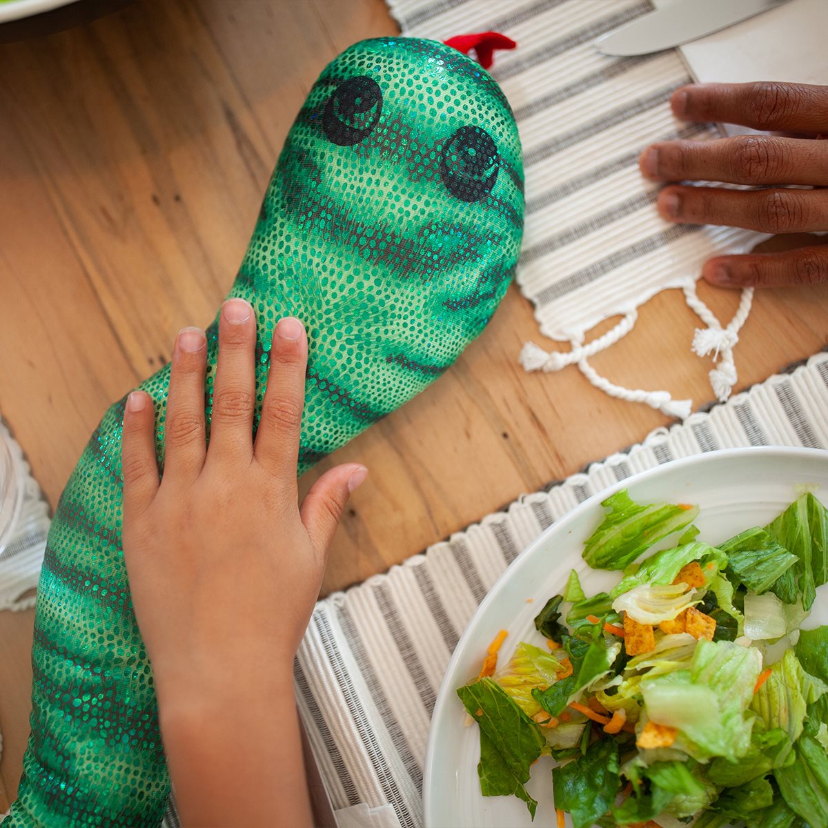 Green manimo snake plush wrapped around a child's body, providing sensory comfort during a quiet moment.