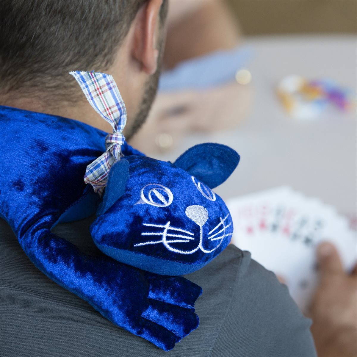 An adult interacting with a 2 kg manimo cat plush while playing cards, illustrating the plush’s use in calming and focusing activities.