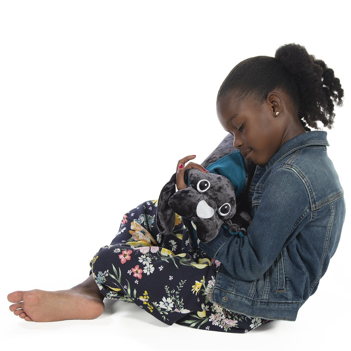 Child sitting with a 1 kg manimo dog plush, using it for sensory comfort in a sitting position.