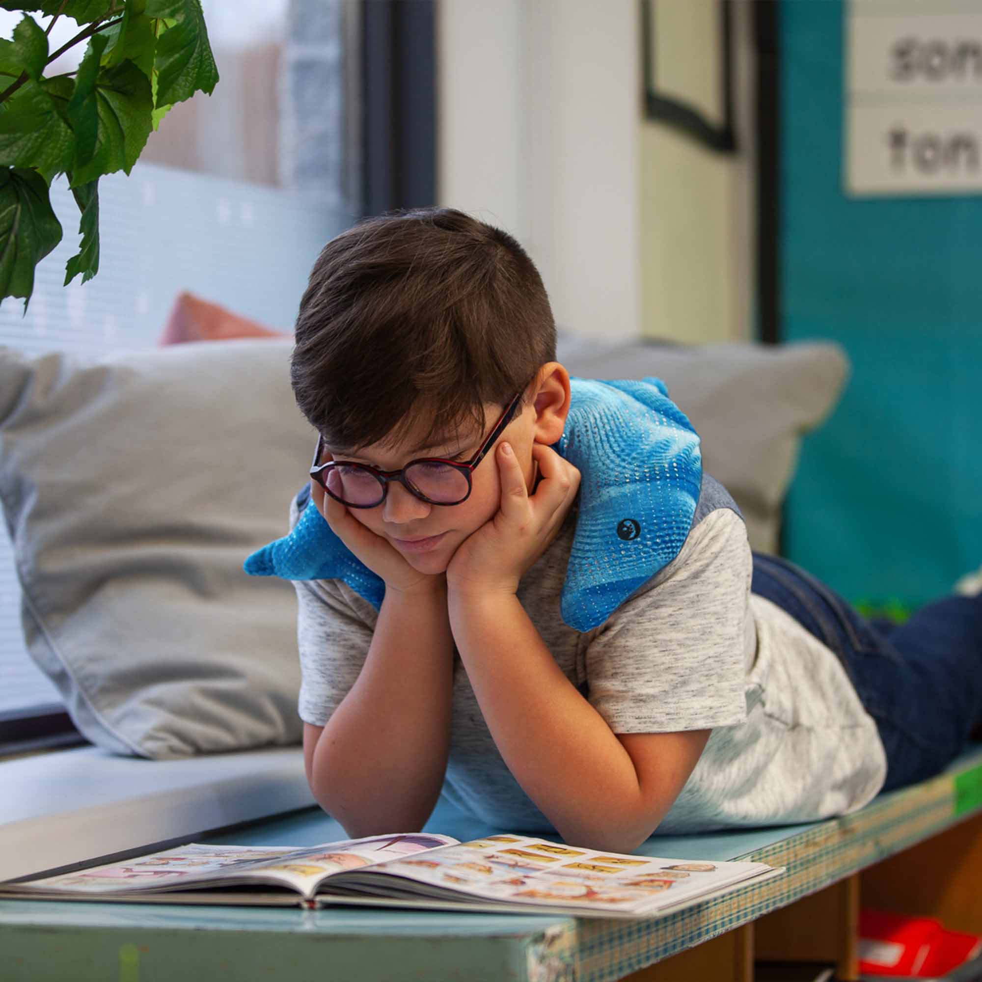 Child holding a blue manimo dolphin plush, demonstrating how it provides comfort and sensory support in a cozy setting.